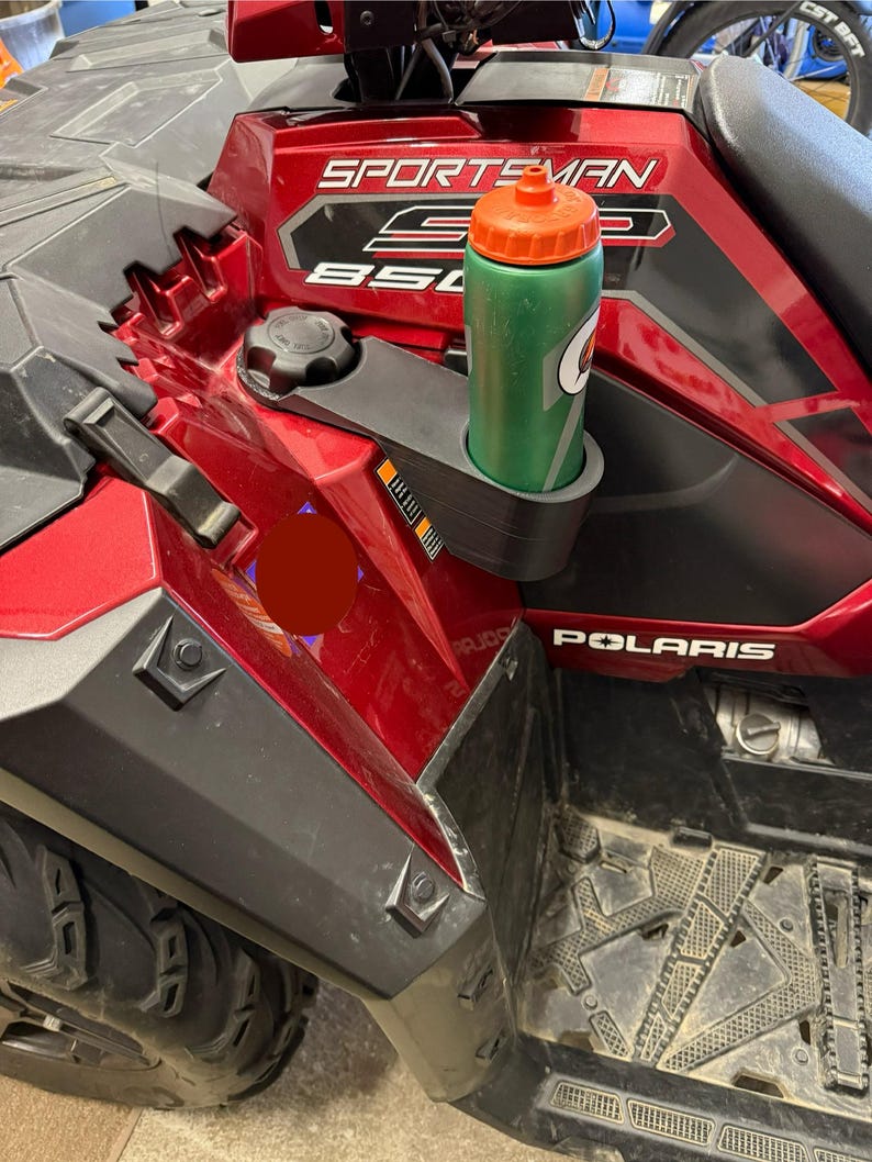 May include: A red and black Polaris Sportsman 850 ATV with a green and orange Gatorade water bottle in the cup holder. The ATV has the word "Sportsman" and "850" printed on the side.