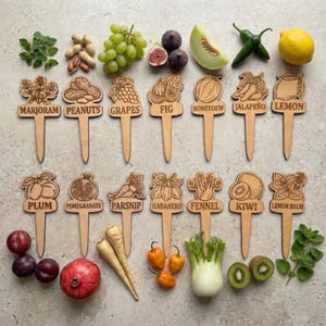May include: A collection of wooden garden markers, each engraved with a different fruit, vegetable, or herb, and its name. Includes marjoram, peanuts, grapes, fig, honeydew, jalapeño, lemon, plum, pomegranate, parsnip, habanero, fennel, kiwi, and lemon balm.