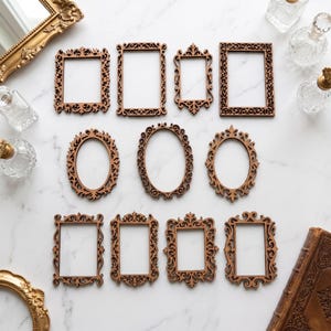 Può includere: Una collezione di cornici decorative in legno di varie forme, tra cui rettangolari e ovali. Le cornici presentano dettagli intagliati intricati e sono disposte su una superficie di marmo bianco. Sono presenti anche bottiglie decorative e un libro d'epoca.