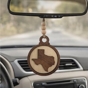 May include: A wooden car air freshener with a Texas state outline. The round ornament is suspended from a string of wooden beads and hangs from a car's rearview mirror. The Texas shape is a darker wood color.