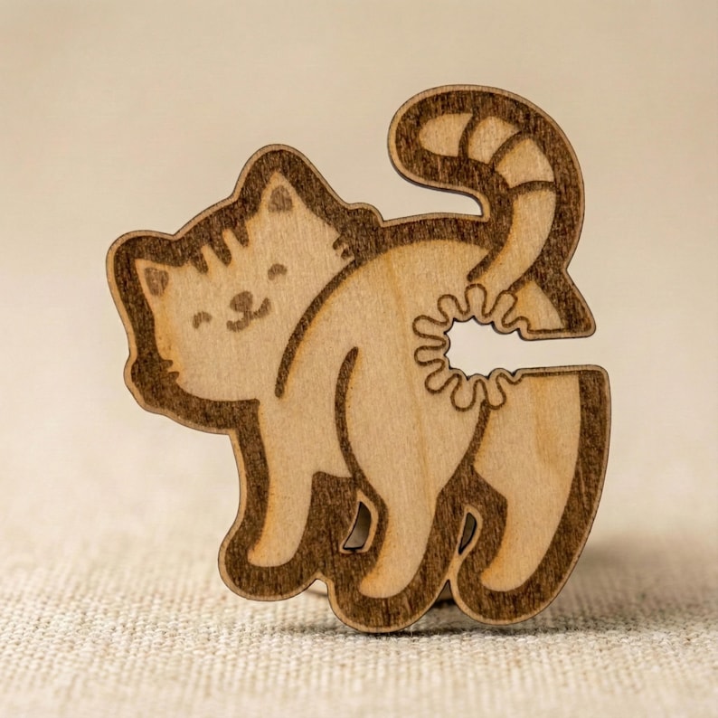 Close-up of a finished wooden laser-cut cat bread tie, featuring engraved details and a smooth, natural wood finish, standing on a textured beige surface.