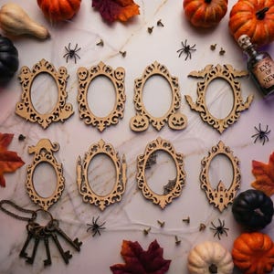 May include: A selection of wooden, oval-shaped Halloween frames with decorative cutouts of bats, pumpkins, and skulls. The frames are displayed with pumpkins, spiders, and autumn leaves, creating a festive seasonal arrangement.