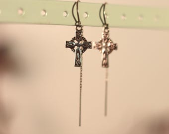 May include: A pair of silver Celtic cross earrings with delicate chains hanging from the bottom. The earrings are displayed against a white background.