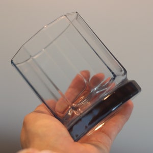 Könnte beinhalten: Ein durchsichtiges Glas mit einem dunkelgrauen Boden. Das Glas hat eine geometrische Form mit mehreren Facetten.