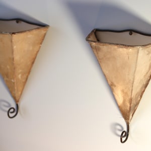 May include: Two brown, triangular wall sconces with metal hooks. The sconces are made of a fabric-like material and have a rustic, vintage look.