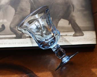 Könnte beinhalten: Ein hellblaues Glasgoblet mit einer breiten Schale und einem kurzen Stiel. Das Goblet hat ein geriffeltes Design und einen klaren Boden.