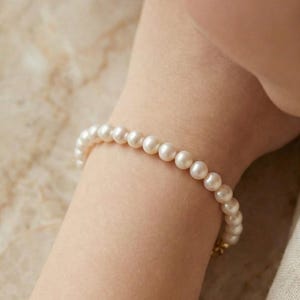 Peut inclure: Un bracelet de perles délicat. Le bracelet est composé d'un rang de perles blanches et rondes. Les perles sont enfilées ensemble, créant un bijou classique et élégant. Le bracelet est porté sur un poignet.