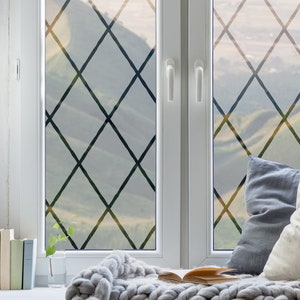 May include: A window with a diamond-shaped grid pattern on the glass. The window is open and there is a view of a mountain range in the distance. A white blanket and pillows are on the window seat.