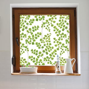 May include: A window with a white background and a green fern pattern. The window is framed in wood and has a white windowsill. There is a small potted plant and a decorative lighthouse on the windowsill.
