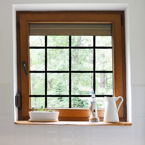 May include: A wooden window with a view of green trees and a white windowsill with a small potted plant, a white pitcher, and a lighthouse figurine.