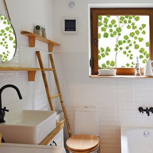 May include: A white bathroom with a white toilet, a white bathtub, a white sink, a wooden ladder, a round mirror with a leafy design, and a window with a leafy design.