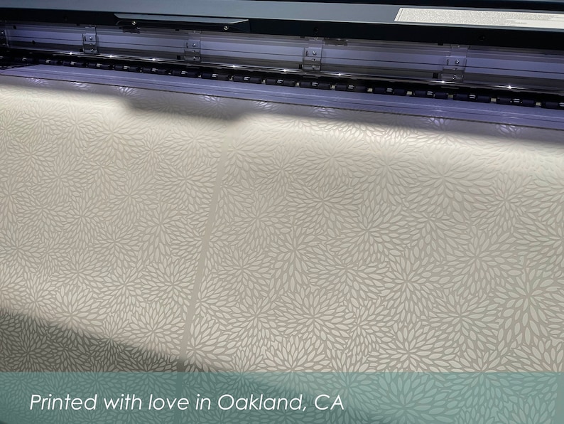 May include: A large format printer printing a white fabric with a delicate floral pattern. The fabric is being printed with a white ink on a light beige background. The text "Printed with love in Oakland, CA" is visible at the bottom of the image.