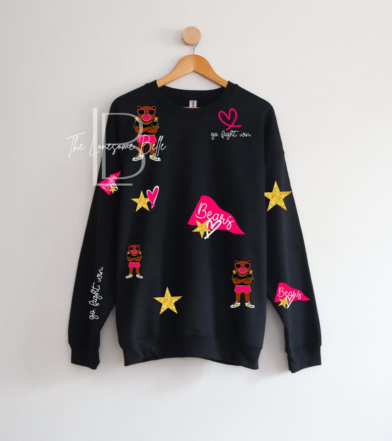 May include: Black sweatshirt with a design featuring a bear wearing sunglasses, stars, hearts, and pennants. The text "go fight win" and "Bears" are also included in the design. The sweatshirt is hanging on a wooden hanger.