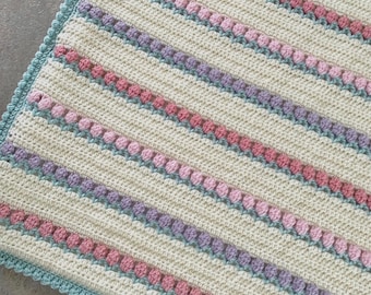 May include: A crocheted baby blanket with a white background and stripes of pink, purple, and blue. The blanket has a crocheted border in a light blue color.