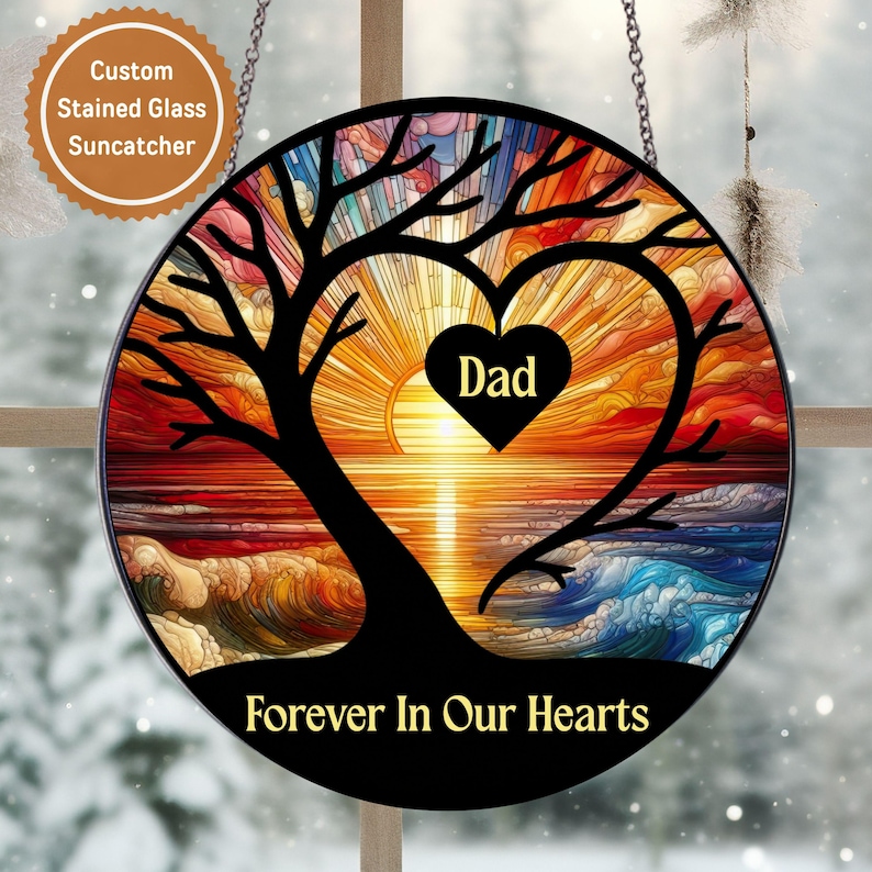 May include: Round stained glass suncatcher with a tree silhouette, heart, and sunset design. The heart contains the word "Dad". The bottom of the suncatcher reads "Forever In Our Hearts". Includes a chain for hanging.