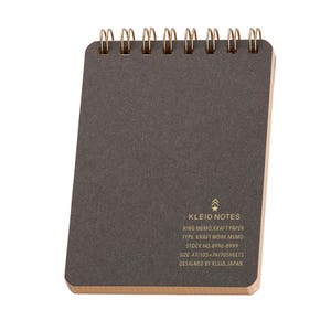 May include: A small, dark gray Kleid Notes ring memo notebook with gold-colored wire binding. The notebook has a kraft paper cover and includes product information printed on the front. The size is A7, approximately 4.1 x 2.9 inches.
