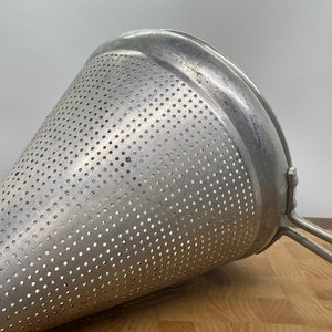 May include: A silver metal cone-shaped strainer with a handle. The strainer has small holes throughout the surface.