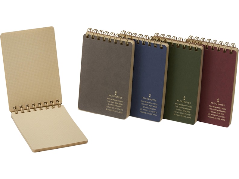 May include: A collection of spiral-bound notebooks in various colors, including gray, blue, green, and burgundy. One notebook is open, revealing grid-lined pages. The notebooks have gold-colored spiral bindings and text on the covers.