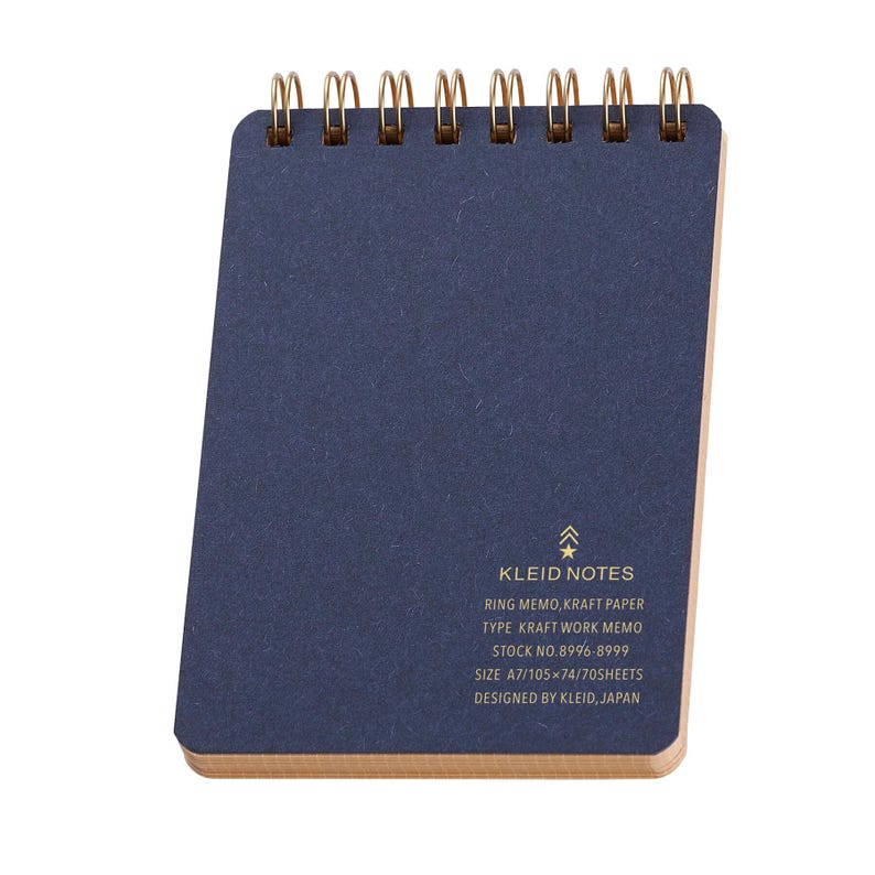 May include: A navy blue Kleid Notes ring memo notepad with gold spiral binding. The notepad has a kraft paper backing and includes the text: RING MEMO, KRAFT PAPER, SIZE A7/105x74/70SHEETS, DESIGNED BY KLEID, JAPAN.