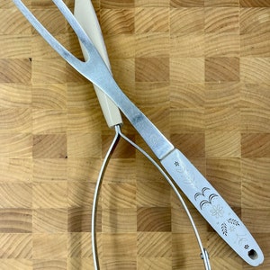 May include: A silver potato masher with a floral design on the handle, sitting on a wooden cutting board.