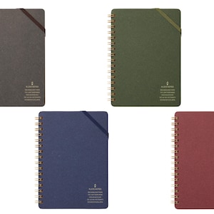 May include: A collection of spiral-bound notebooks in various colors: charcoal, olive green, navy blue, and burgundy. Each notebook features a gold spiral binding, a matching elastic closure, and a small printed logo with text.