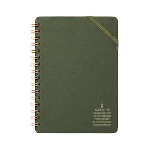 May include: A green spiral-bound notebook with gold-colored metal rings and an elastic band closure. The notebook has the text "KLEID NOTES" and other details printed on the bottom right corner. The notebook is A6 size and contains 70 sheets.