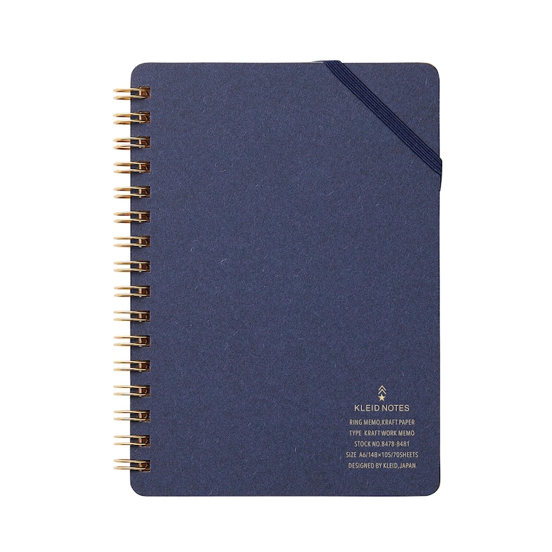 May include: A navy blue spiral-bound notebook with gold-colored metal rings. The notebook has an elastic band closure and the text "KLEID NOTES" is printed on the bottom right corner. The notebook is designed in Japan.