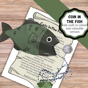 May include: A green paper fish craft with a dark green head and a white eye is placed on a printed page with text. A coin is attached to the fish with string. The text "COIN IN THE FISH" is in a black and white circle.