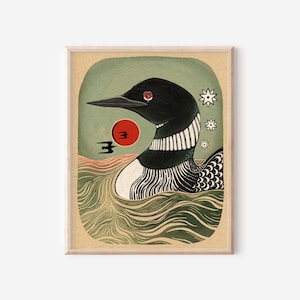 May include: A framed art print featuring a stylized black and white loon swimming in wavy green water. A red sun, two small black birds, and three white star-like shapes are positioned near the loon against a muted green background.