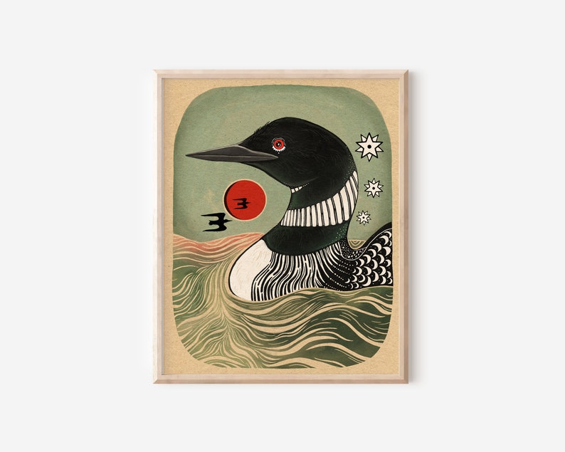 May include: A framed art print featuring a stylized black and white loon swimming in wavy green water. A red sun, two small black birds, and three white star-like shapes are positioned near the loon against a muted green background.