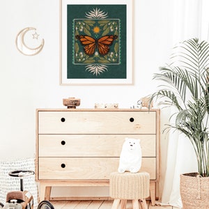 K&ouml;nnte beinhalten: Ein t&uuml;rkisfarbener gerahmter Druck mit einer Schmetterlings-Illustration. Der Schmetterling ist orange und schwarz mit einer gelben Sonne und wei&szlig;en Blumen im Hintergrund.