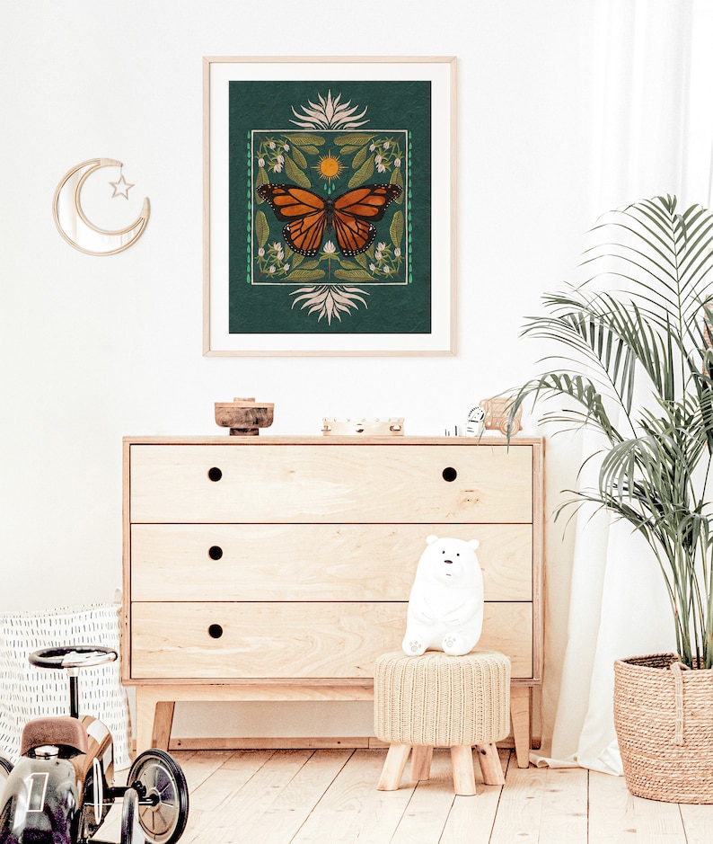 K&ouml;nnte beinhalten: Ein t&uuml;rkisfarbener gerahmter Druck mit einer Schmetterlings-Illustration. Der Schmetterling ist orange und schwarz mit einer gelben Sonne und wei&szlig;en Blumen im Hintergrund.