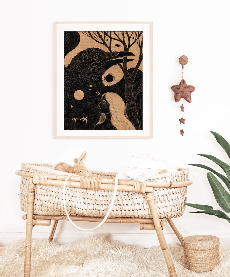 May include: A black and white illustration of a woman and a raven in a forest setting. The illustration is framed in a light wood frame and hangs on a white wall. A brown star-shaped mobile hangs from the wall above the frame.
