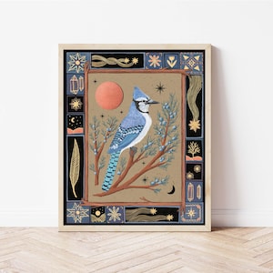 May include: Framed art print featuring a blue jay perched on a branch. The artwork has a tan background with a red sun and celestial elements. The border is dark blue with gold accents, creating a whimsical, nature-inspired design.