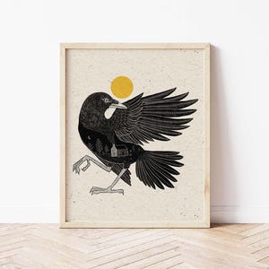 May include: Framed art print featuring a stylized black crow with outstretched wings, a yellow sun, and a small house illustration. The artwork is set against a textured, off-white background, and framed in light wood.