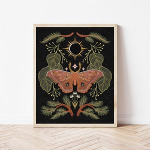 May include: A framed art print featuring a detailed illustration of a moth with outstretched wings, set against a black background. The moth is in shades of orange and brown, surrounded by botanical elements in green and gold. The artwork has a vintage, nature-inspired theme.