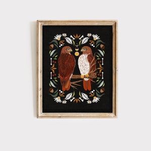 May include: A framed print of two red-tailed hawks perched on a branch, surrounded by a decorative border of leaves, flowers, and acorns on a black background.
