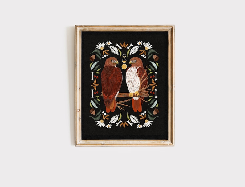 May include: A framed print of two red-tailed hawks perched on a branch, surrounded by a decorative border of leaves, flowers, and acorns on a black background.