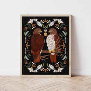 May include: A digital illustration of two red-tailed hawks perched on a branch, surrounded by a decorative border of leaves, flowers, and bones. The background is black.