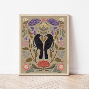May include: A digital illustration of two black birds facing each other with their beaks touching, forming a heart shape. The birds are surrounded by a wreath of colorful flowers and leaves on a beige background.