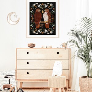 May include: A framed illustration of two red-tailed hawks perched on a branch, surrounded by a decorative border of leaves, flowers, and other natural elements. The background is black.