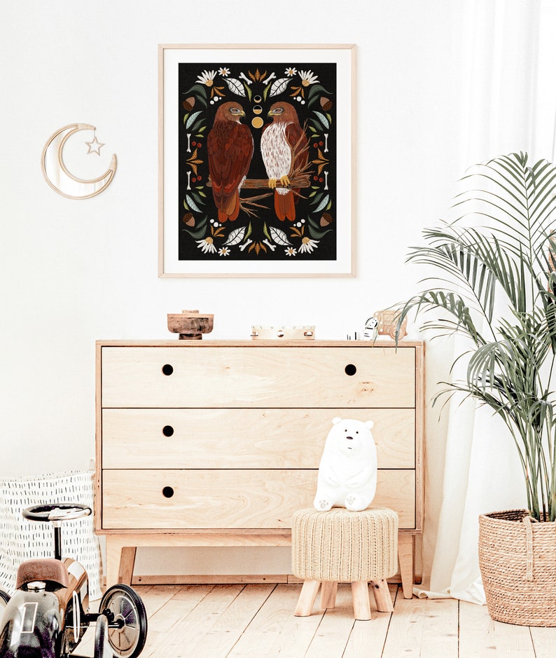 May include: A framed illustration of two red-tailed hawks perched on a branch, surrounded by a decorative border of leaves, flowers, and other natural elements. The background is black.