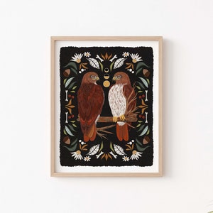 May include: A framed print of two red-tailed hawks perched on a branch, surrounded by a black background with a floral pattern. The print features a stylized design with a folk art aesthetic.