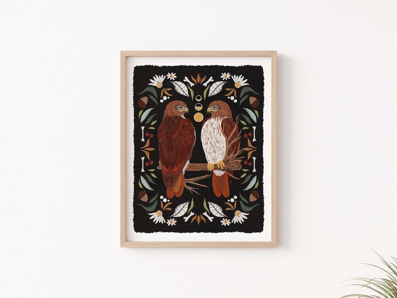 May include: A framed print of two red-tailed hawks perched on a branch, surrounded by a black background with a floral pattern. The print features a stylized design with a folk art aesthetic.