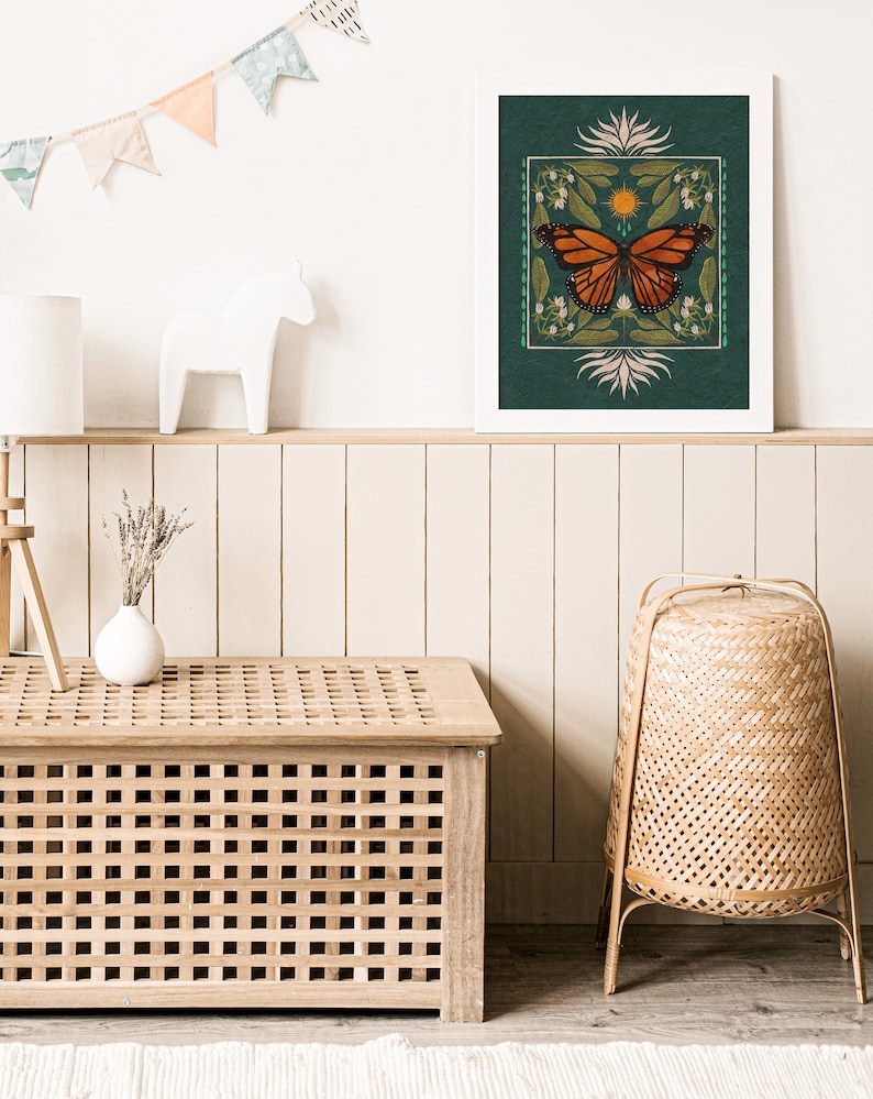 K&ouml;nnte beinhalten: Ein gerahmter Druck eines Monarchfalters mit gr&uuml;nem Hintergrund und floralen Akzenten. Der Schmetterling ist orange und schwarz mit wei&szlig;en Flecken. Der Druck ist in einem wei&szlig;en Rahmen und h&auml;ngt an einer wei&szlig;en Wand.