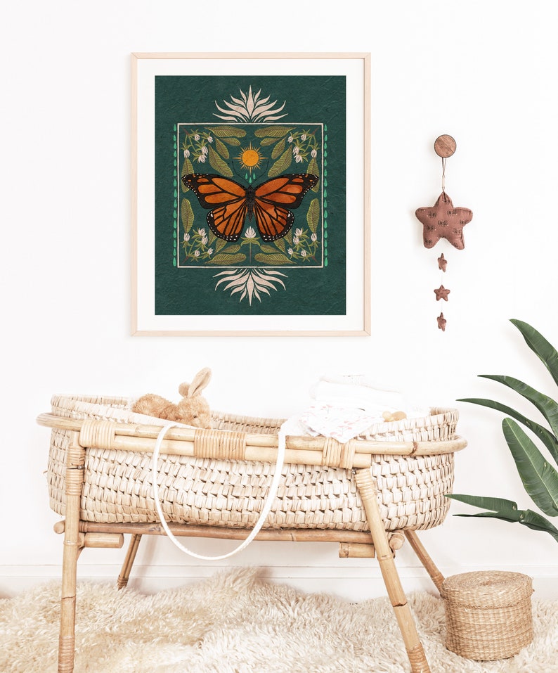 K&ouml;nnte beinhalten: Ein gerahmter Druck eines Schmetterlings mit gr&uuml;nem Hintergrund und floralen Akzenten. Der Druck h&auml;ngt an einer wei&szlig;en Wand &uuml;ber einer Weidenwiege.