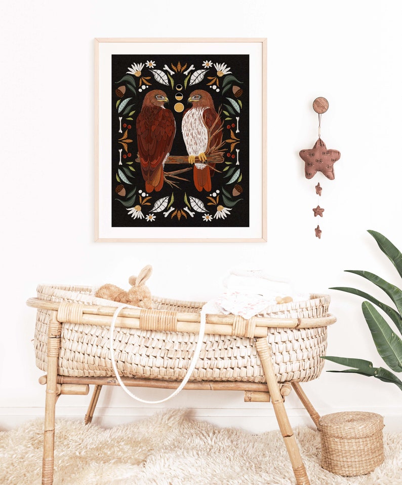 May include: A framed illustration of two red-tailed hawks perched on a branch, surrounded by a border of leaves, flowers, and acorns. The background is black, and the image has a rustic, vintage feel.