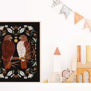 May include: A framed print with a black background featuring two red-tailed hawks perched on a branch. The hawks are surrounded by a border of stylized floral and botanical elements in shades of green, brown, and white.