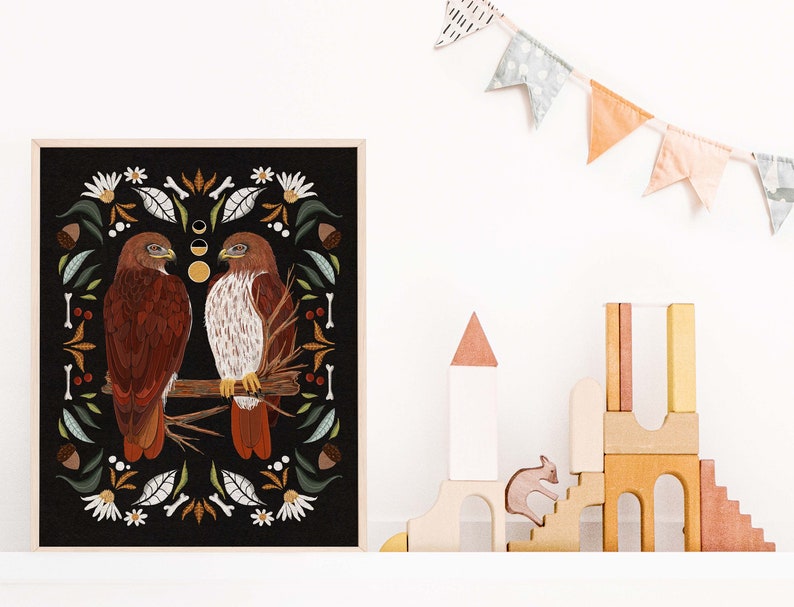 May include: A framed print with a black background featuring two red-tailed hawks perched on a branch. The hawks are surrounded by a border of stylized floral and botanical elements in shades of green, brown, and white.