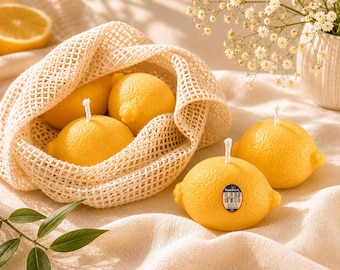Puede incluir: Varias velas amarillas con forma de limón con mechas blancas, algunas dentro de una bolsa de malla beige. Una vela tiene una etiqueta "Sunkist". También hay un limón en rodajas y un jarrón con flores blancas.